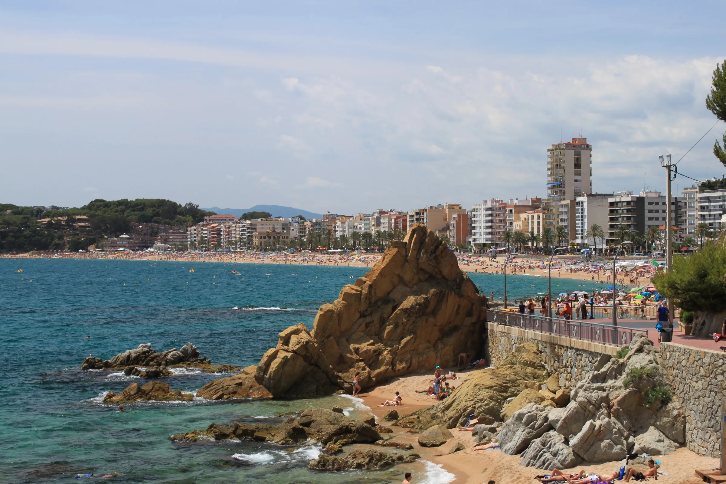 Baai en zandstrand van Lloret de Mar met markante kustrots, palmenboulevard en appartementen aan de Costa Brava
