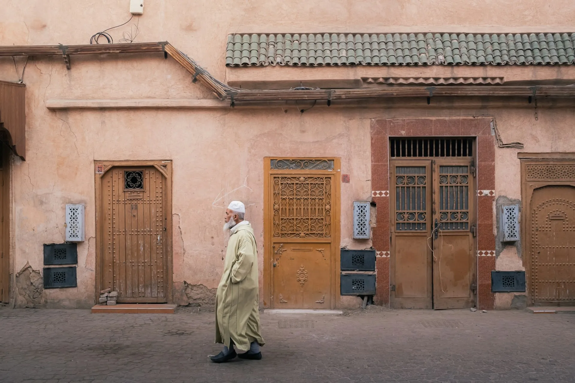 Oudere man in djellaba loopt langs traditionele houten deuren in de medina van Marrakech