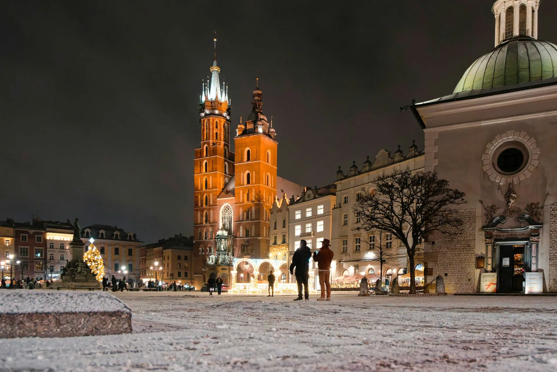 Rynek Główny in Krakau bij avond, met de verlichte torens van de Mariakerk in de sneeuw