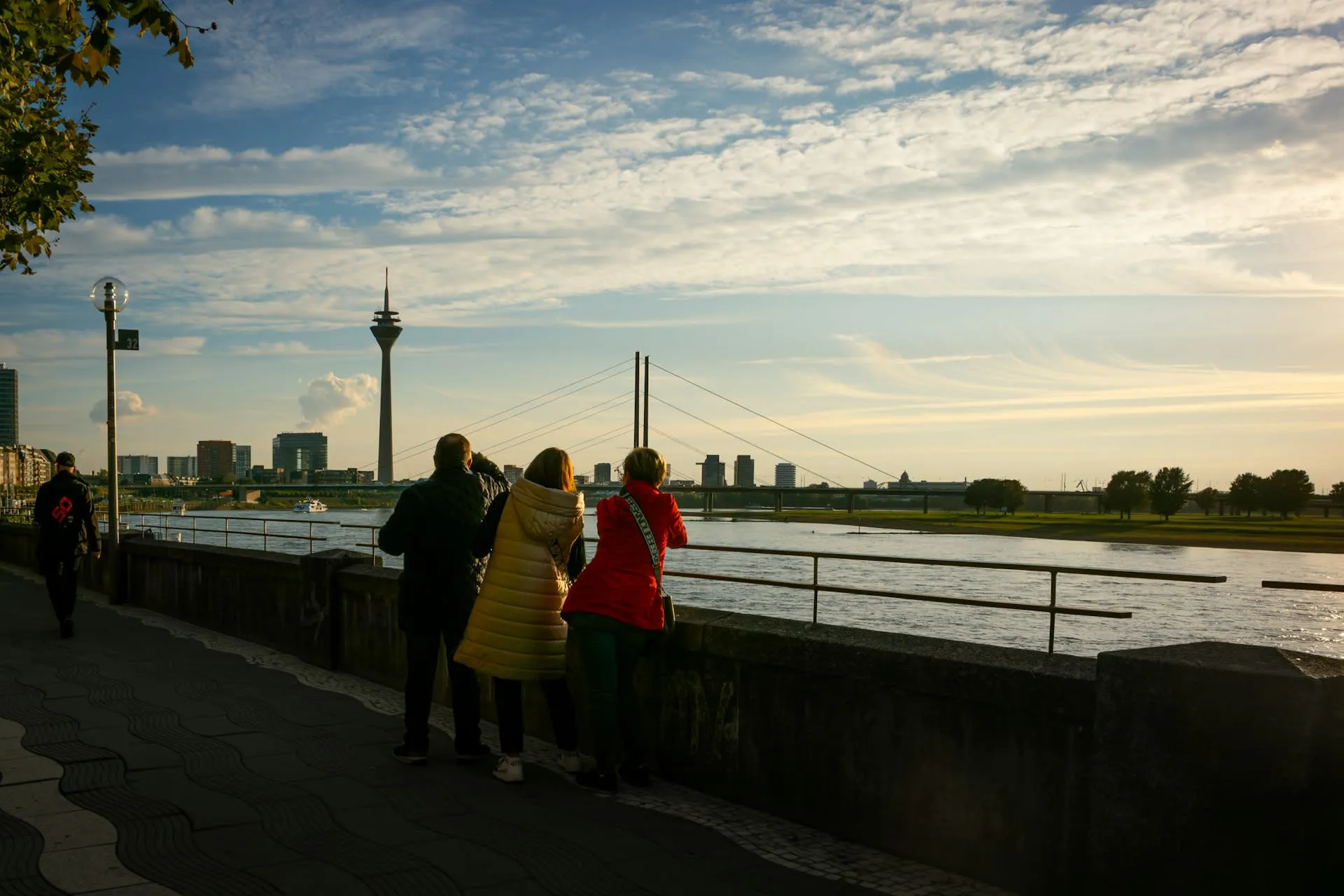 Toeristen bij de Rijnpromenade in Düsseldorf met de Rheinturm en Rijnkniebrücke in gouden avondlicht