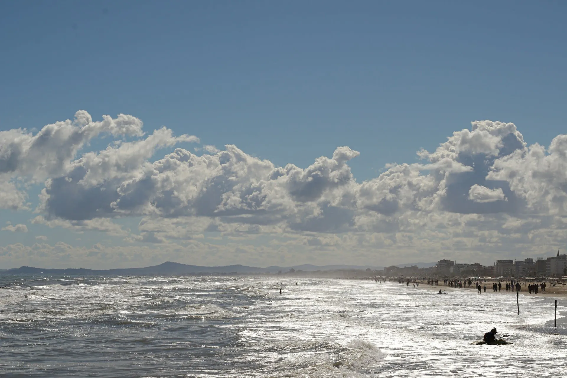 Brede zandkust van Rimini met branding, wolkenlucht en de skyline van de badplaats in de verte