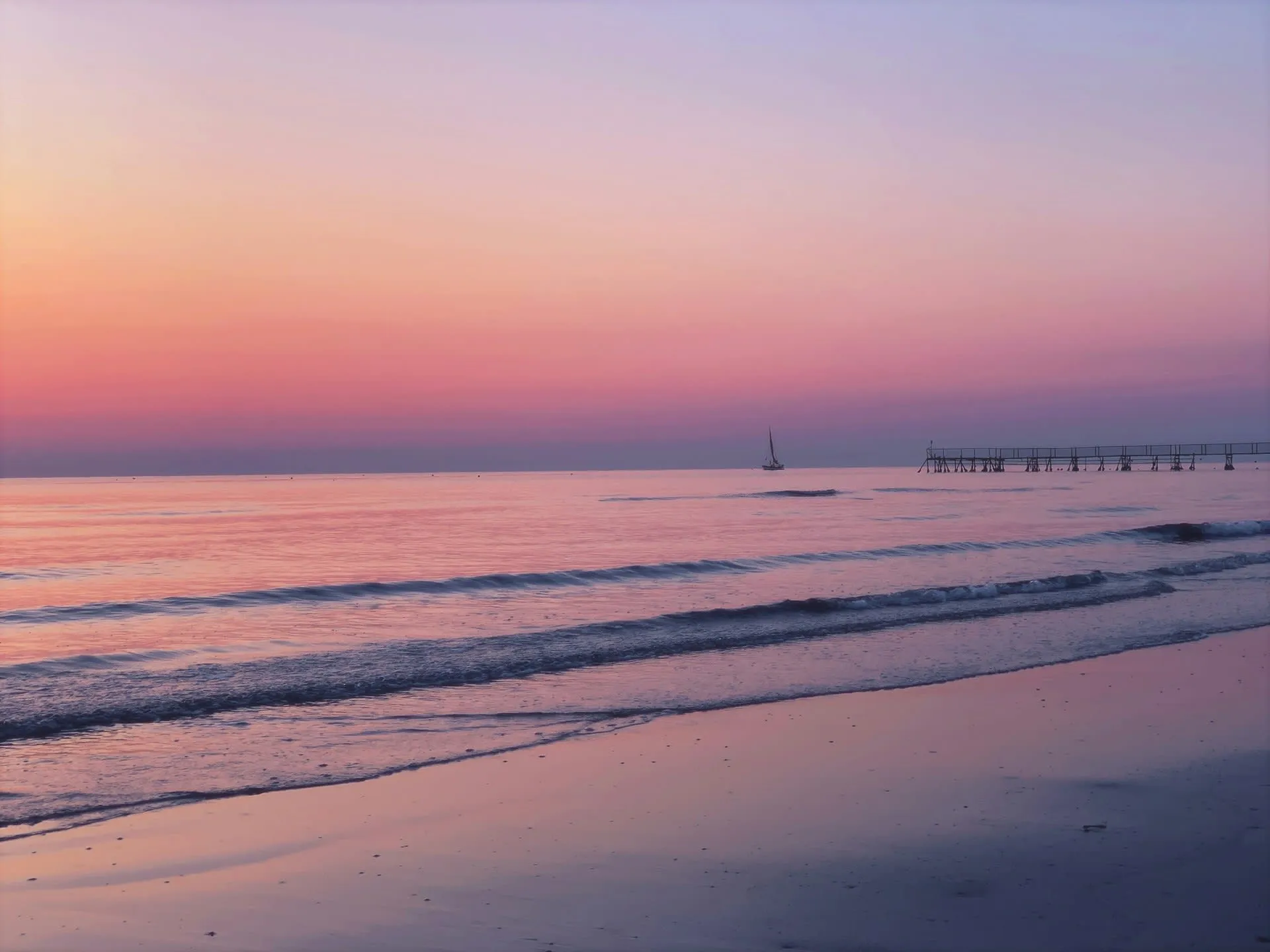 Zonsondergang boven de Adriatische Zee bij Rimini met zeilboot en pier in roze avondlicht